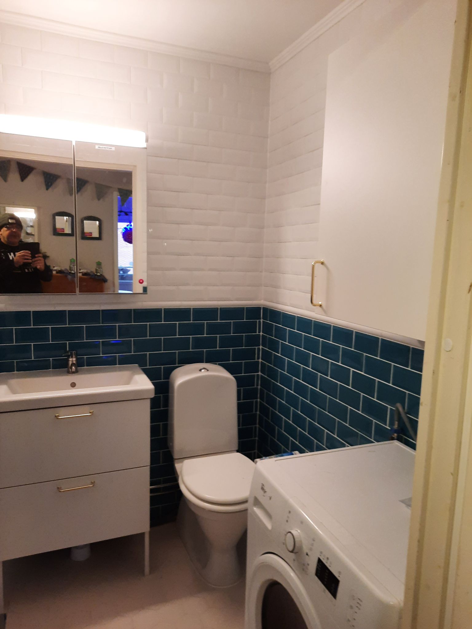 Badrum med blått kakel, tvättmaskin och toalett