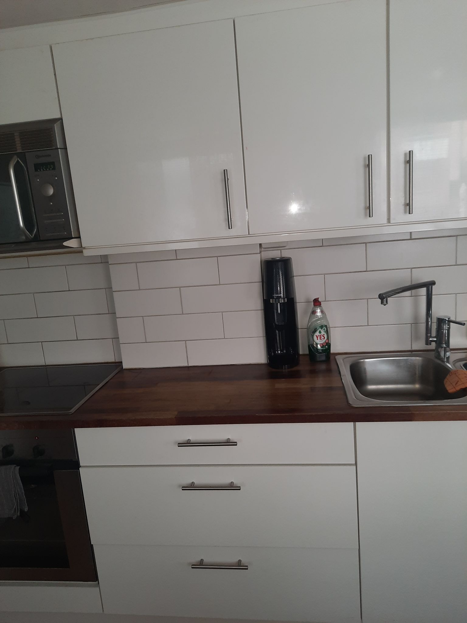Kök med vita luckor, mörk träbänkskiva och vitt kakel