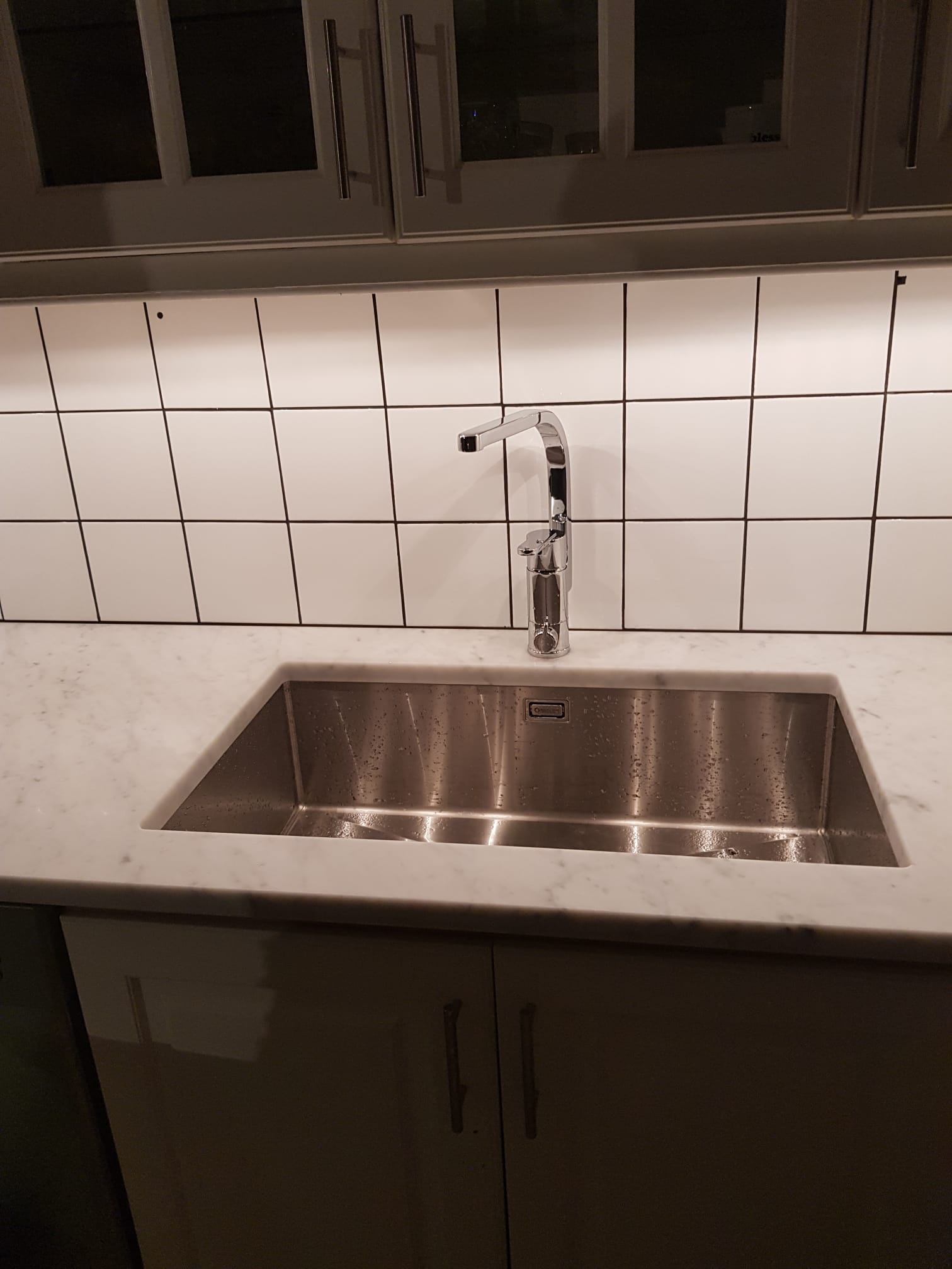 Köksdiskho med marmorskiva, blandare och vitt kakel