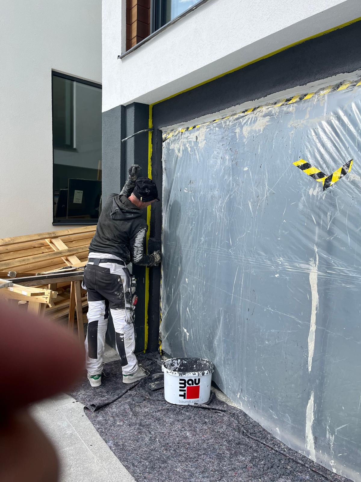 Målare arbetar med mörkgrå fasad vid garageport